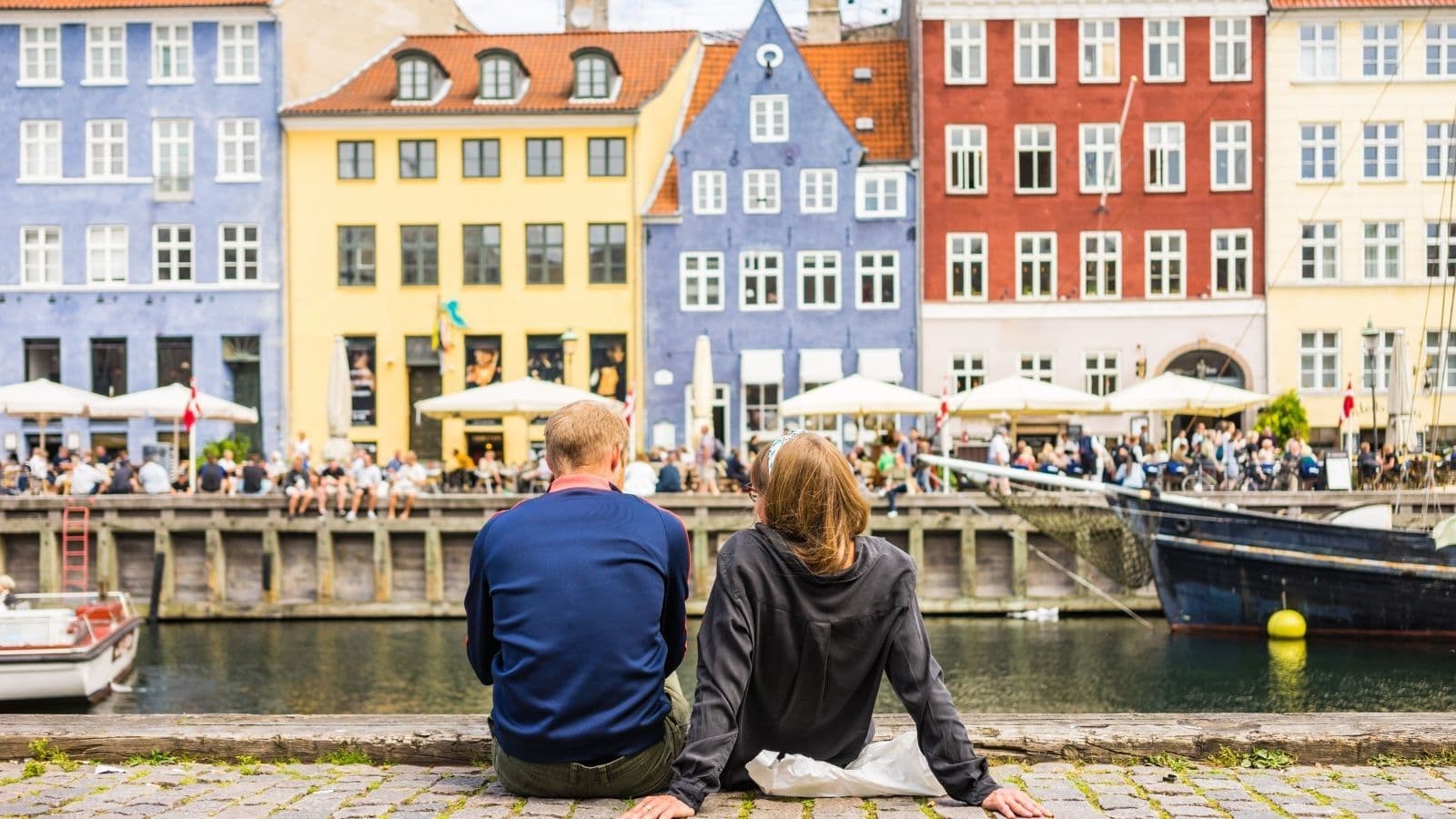 Man and woman sitting and relaxing by the canal in Nyhavn in Copenhagen