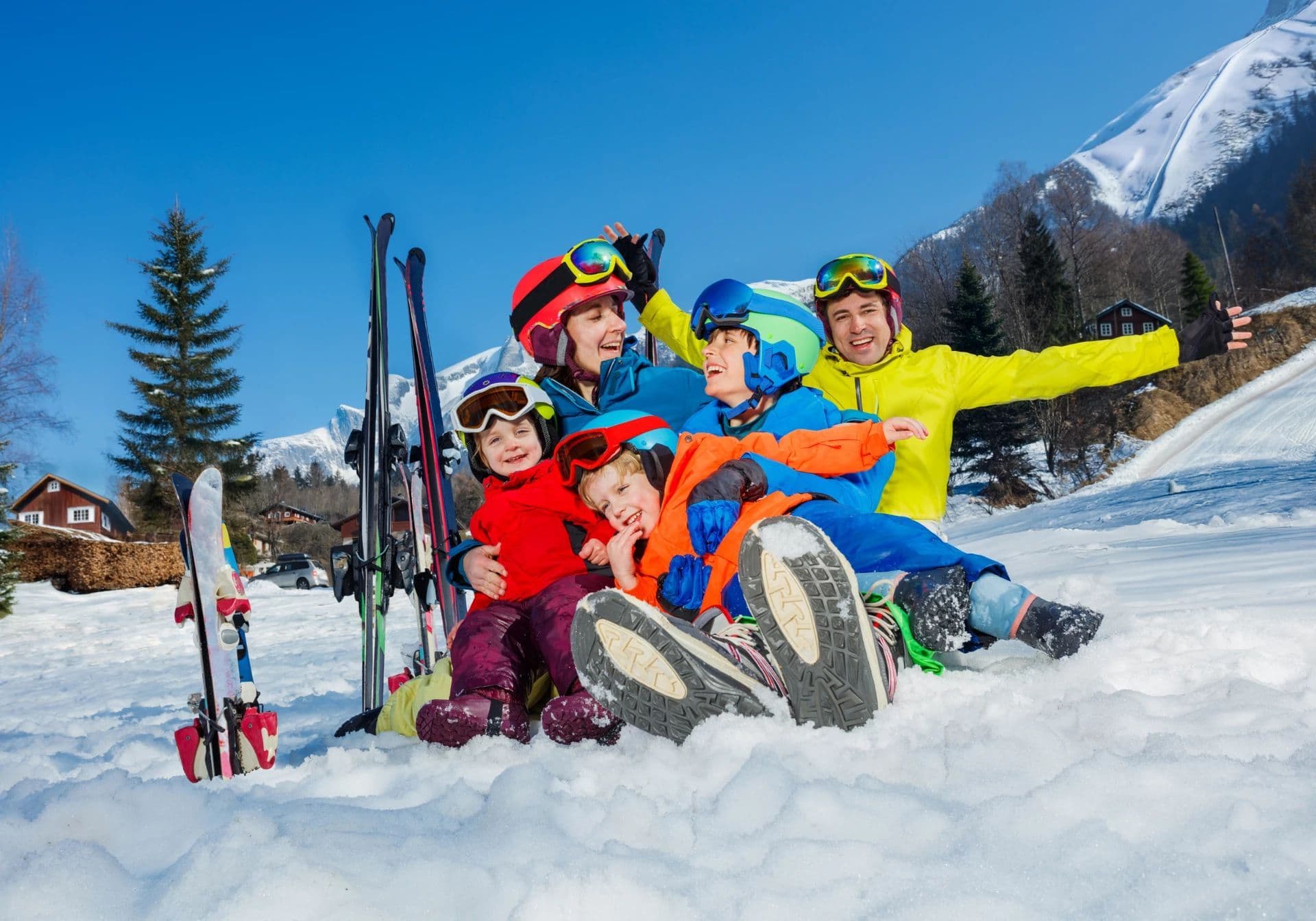 Glad familie sidder i sneen med skiudstyr på